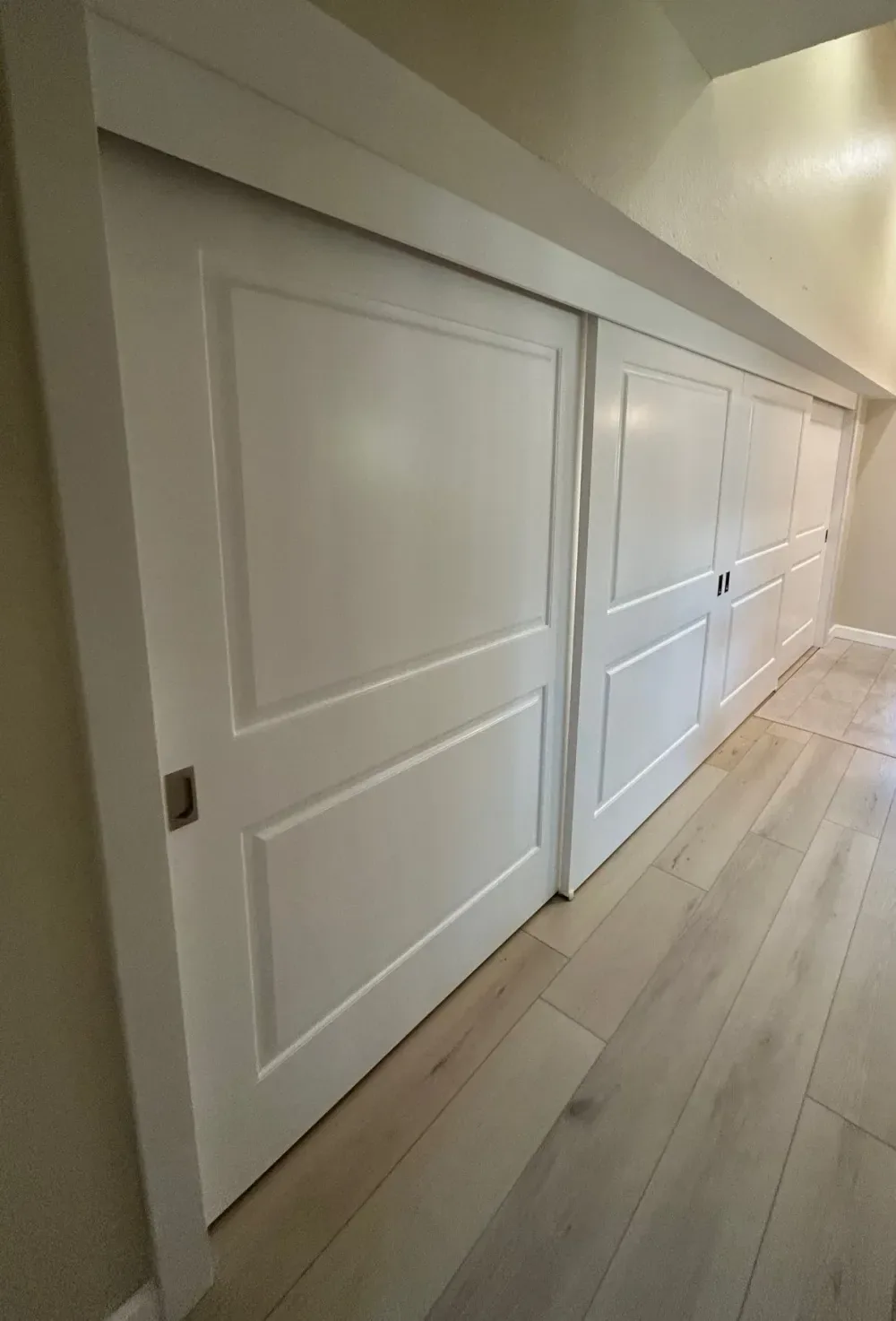 A run of white two-panel square-top sliding bypass closet doors along a hallway