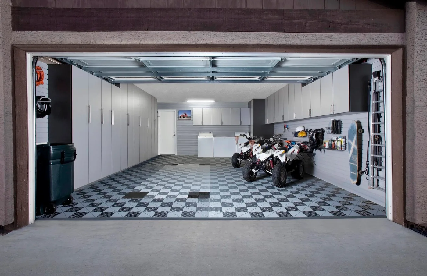 Two-car garage with slate silver storage cabinets, checkered floor tile and ATVs parked inside