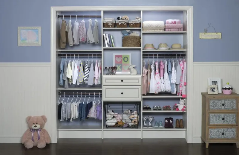 Antique white reach-in closet designed for a baby girl's nursery, with baskets, hanging storage and folded linens