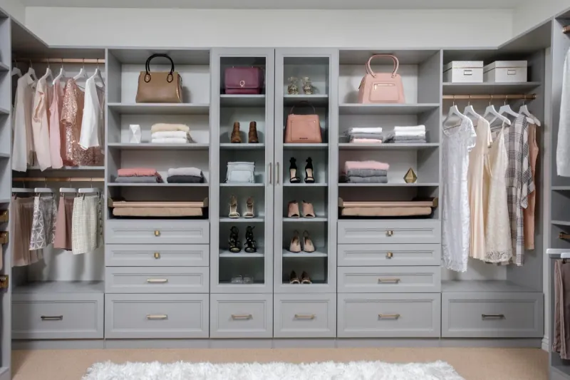 Boutique-style walk-in closet in cloud gray finish with glass-front cabinets, gold hardware and handbag display shelving