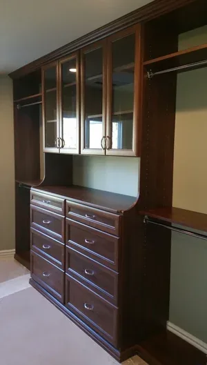 Rich wood-tone walk-in closet with glass cabinet doors and drawer stack